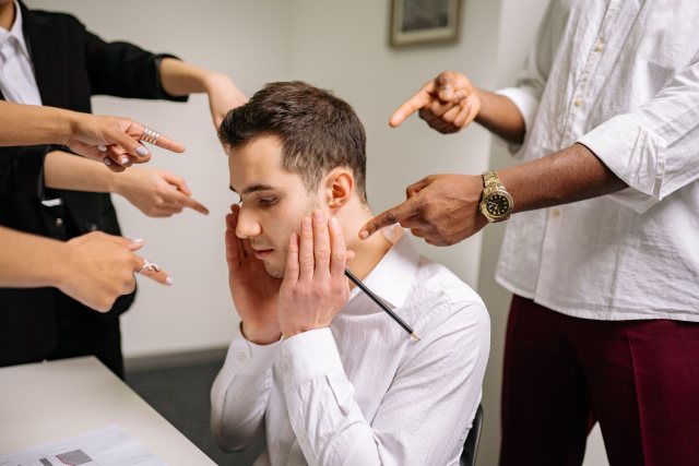 A stressed man at the office surrounded by pointing fingers