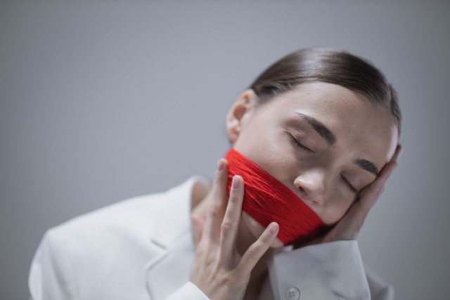 Conceptual portrait of a woman with a red cloth gag on a white background.